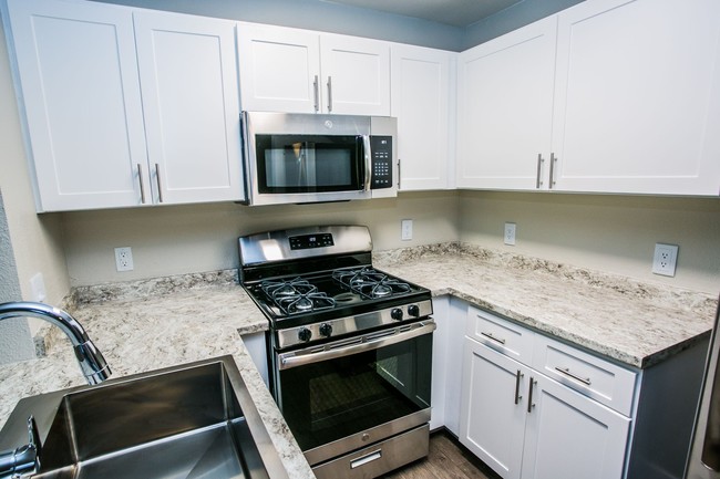 Stainless steel microwave and gas range with white shaker cabinets, granite counter, and large sink. - The Lido Apartments